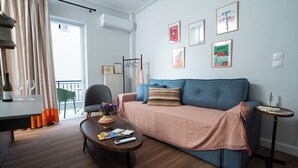 A modern living room with a sofa, coffee table, and a small side table. There are framed pictures on the wall and a window with curtains. - Modern & Sunny apartment with Garden View in the heart of the city center NYX 1 (Tripoli)