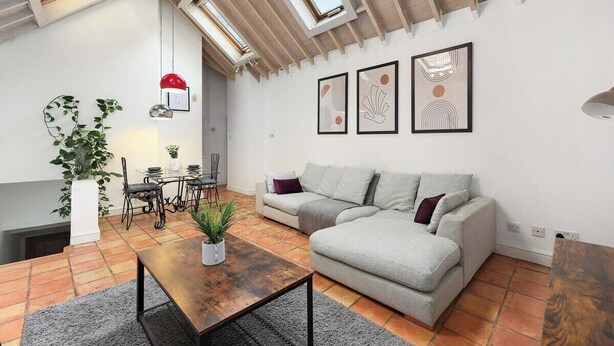 A living room with a sofa, a coffee table, a dining table with chairs, a potted plant, and artwork on the wall. - Cozy private 1-bedroom apartment in Hoxton (Greater London)