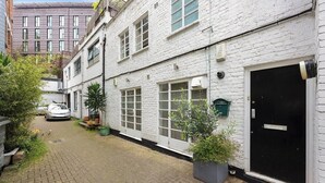 A narrow alleyway with a white brick building, a black door, and a parked car. - Cozy private 1-bedroom apartment in Hoxton (Greater London)