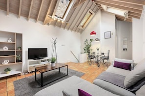 A modern living room with a TV, sofa, coffee table, and a dining area with a table and chairs.