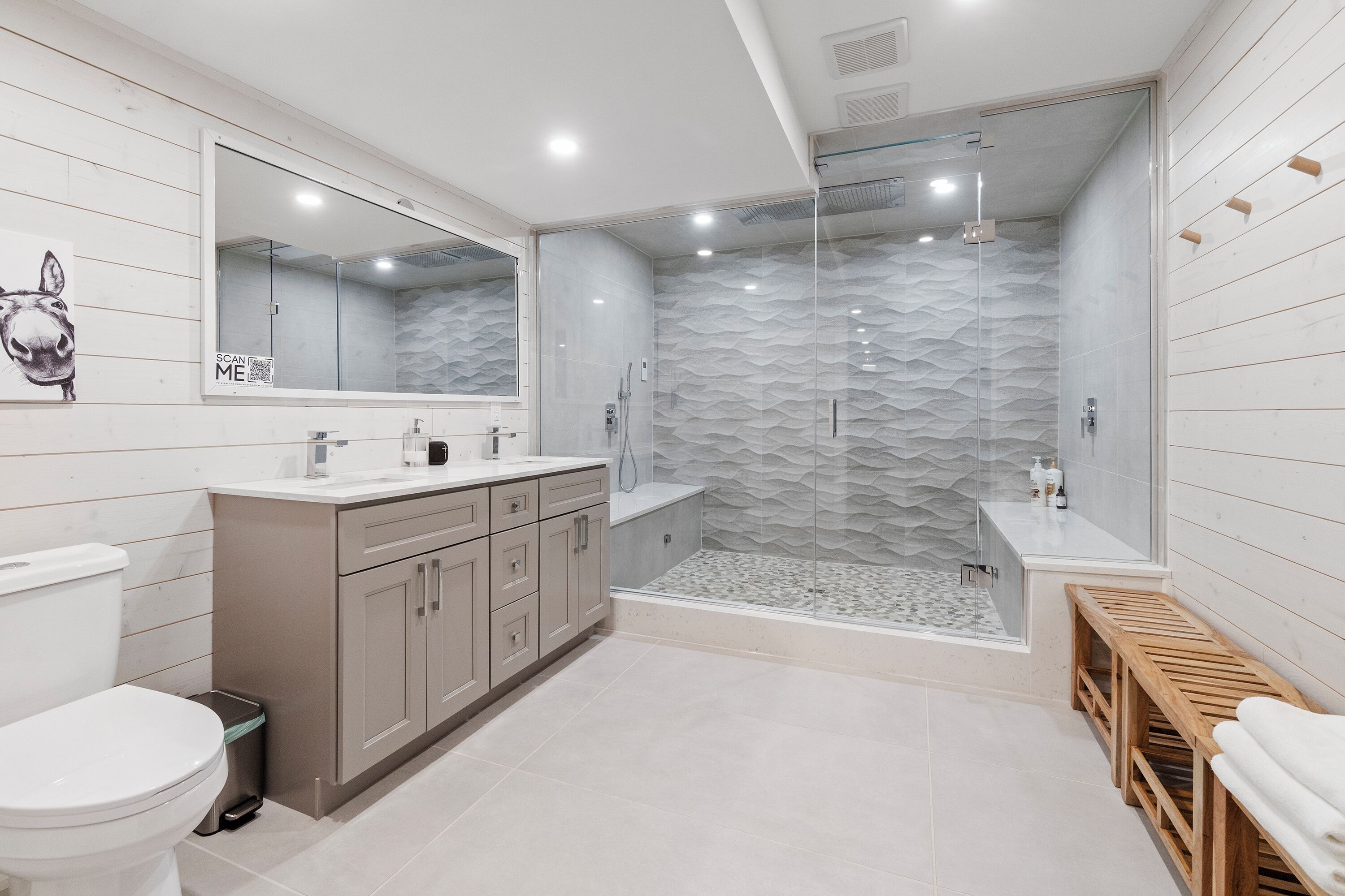 Un baño moderno con ducha acristalada, un espejo grande y un banco de madera.
