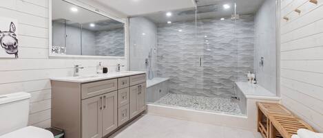 Un baño moderno con ducha acristalada, un espejo grande y un banco de madera.