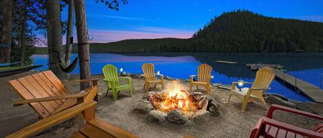 Un feu de camp au bord du lac, avec des chaises en bois et un hamac.