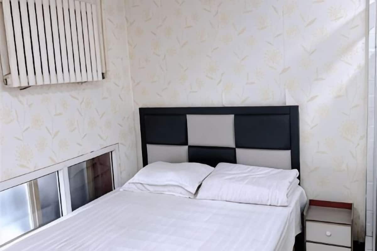 A bed with a black and white headboard, a bedside table with a drawer, and a window with blinds.