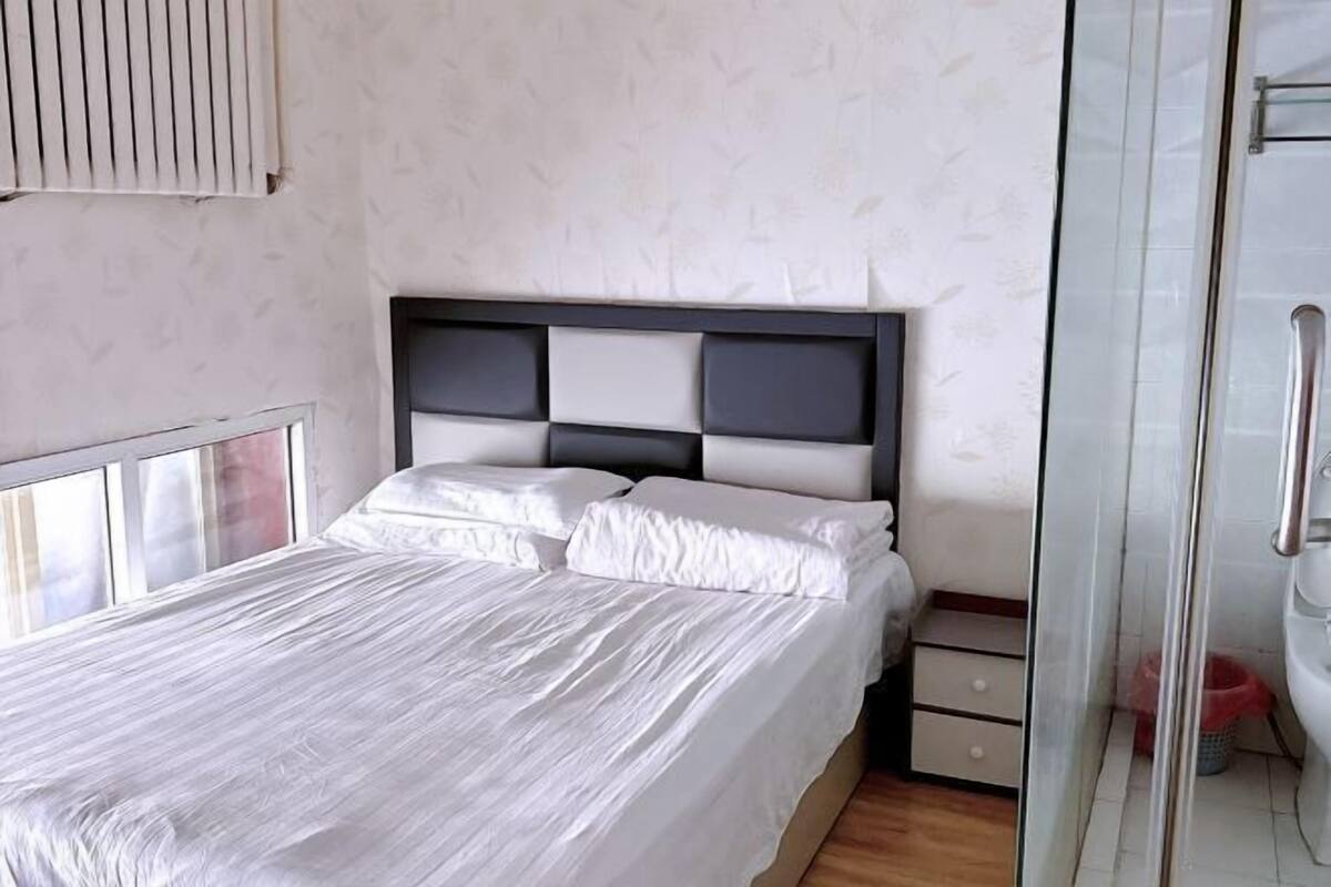 A bedroom with a bed, a bedside table, and a glass shower enclosure.