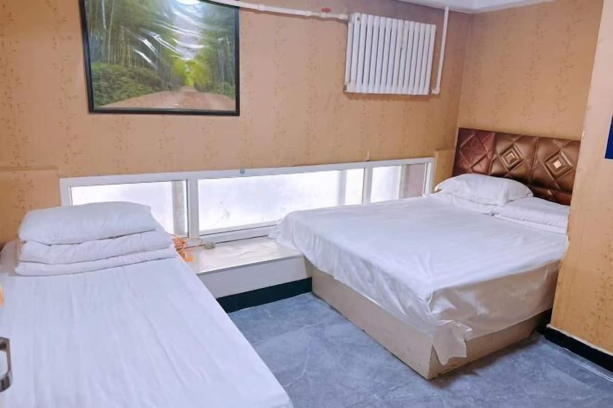 A hotel room with two beds, a window with blinds, a radiator, and a picture on the wall.
