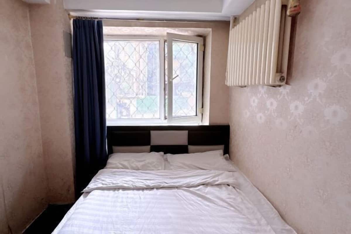 A small, single-bed room with a window, a radiator, and a curtain.