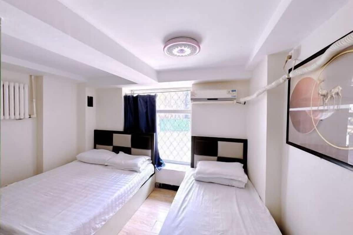 A room with two beds, a window with curtains, a ceiling light, and a wall-mounted air conditioning unit.