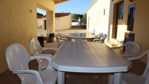 Une terrasse extérieure avec une table ronde et des chaises en plastique blanches.
