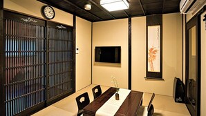 A traditional Japanese-style room with tatami flooring, a low table with a vase of flowers, a clock, and a sliding door with vertical bars.