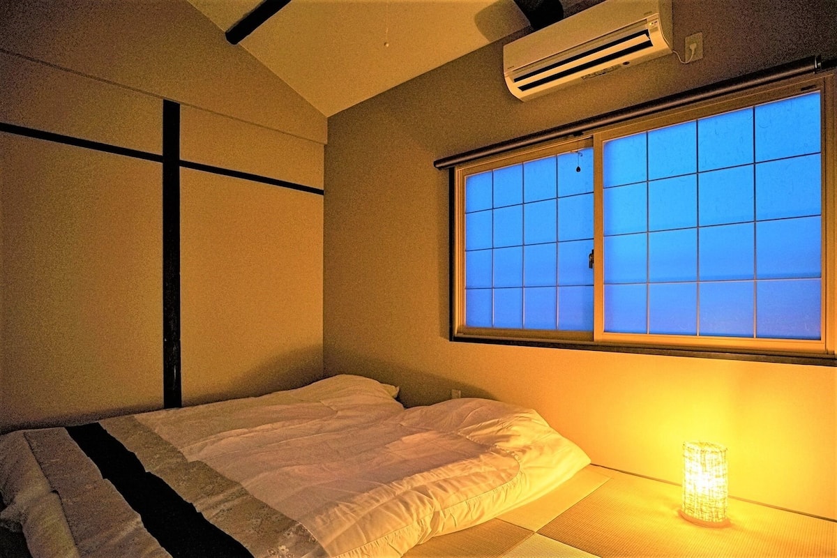 A bedroom with a bed, a window with blue-tinted glass, and a bedside table with a lamp.