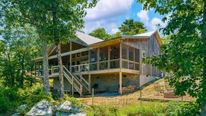 Eine moderne Holzhütte mit einer großen Terrasse, zahlreichen Fenstern und einer Treppe, die zum Obergeschoss führt.