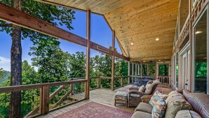 Eine überdachte Terrasse im Freien mit Holzbalken, einer gepolsterten Sitzecke und Blick auf den umliegenden Wald.