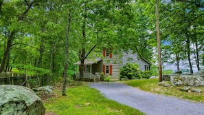 A rustic cabin surrounded by dense forest, with a gravel path leading to the entrance.