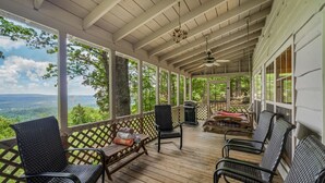 Une véranda couverte avec des fauteuils en osier, une table en bois et un barbecue.
