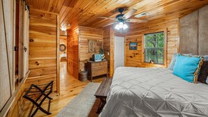 Une chambre confortable dans un chalet en rondins, avec un lit, un banc, une commode et un ventilateur de plafond.