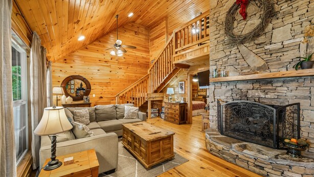 L’intérieur chaleureux d’un chalet en bois, avec une cheminée en pierre, un escalier en bois et un coin salon confortable.