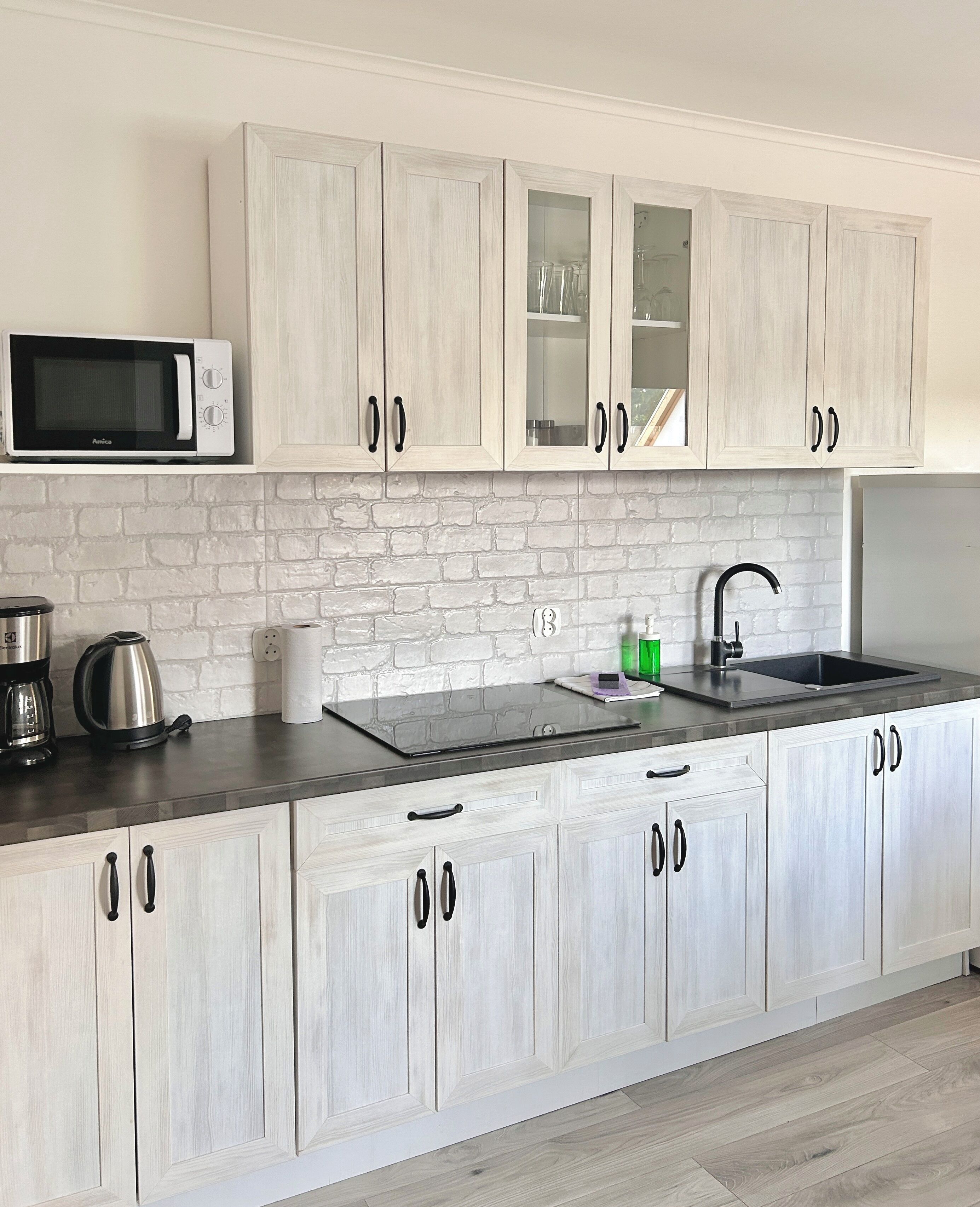 Een moderne keuken met lichte houten kastjes, een magnetron, een waterkoker, een broodrooster en een spoelbak.