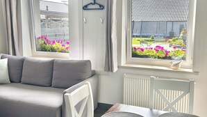 A cozy room with a grey sofa, a dining table with placemats, and a view of a garden through large windows. - Apartamenty Golf Dyndeby (Nexø)