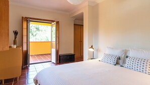 Une chambre avec un grand lit, une table de chevet, une lampe, une armoire en bois et une porte donnant sur un espace extérieur.