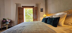 A bedroom with a bed, a nightstand, a lamp, and a view of greenery outside. - Country Rental Home Genalguacil Jubrique. Hiking, Biking, Nature, White Villages (Jubrique)