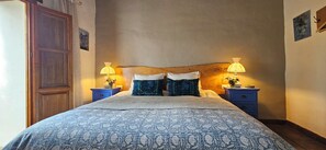 A bedroom with a large bed, two bedside tables with lamps, a wooden headboard, and a door. - Country Rental Home Genalguacil Jubrique. Hiking, Biking, Nature, White Villages (Jubrique)