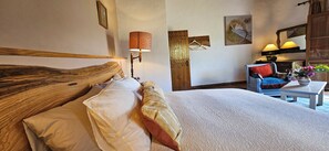 Een hotelkamer met een groot bed, een houten hoofdbord, een tafeltje met een vaas en een stoel met een kussen.