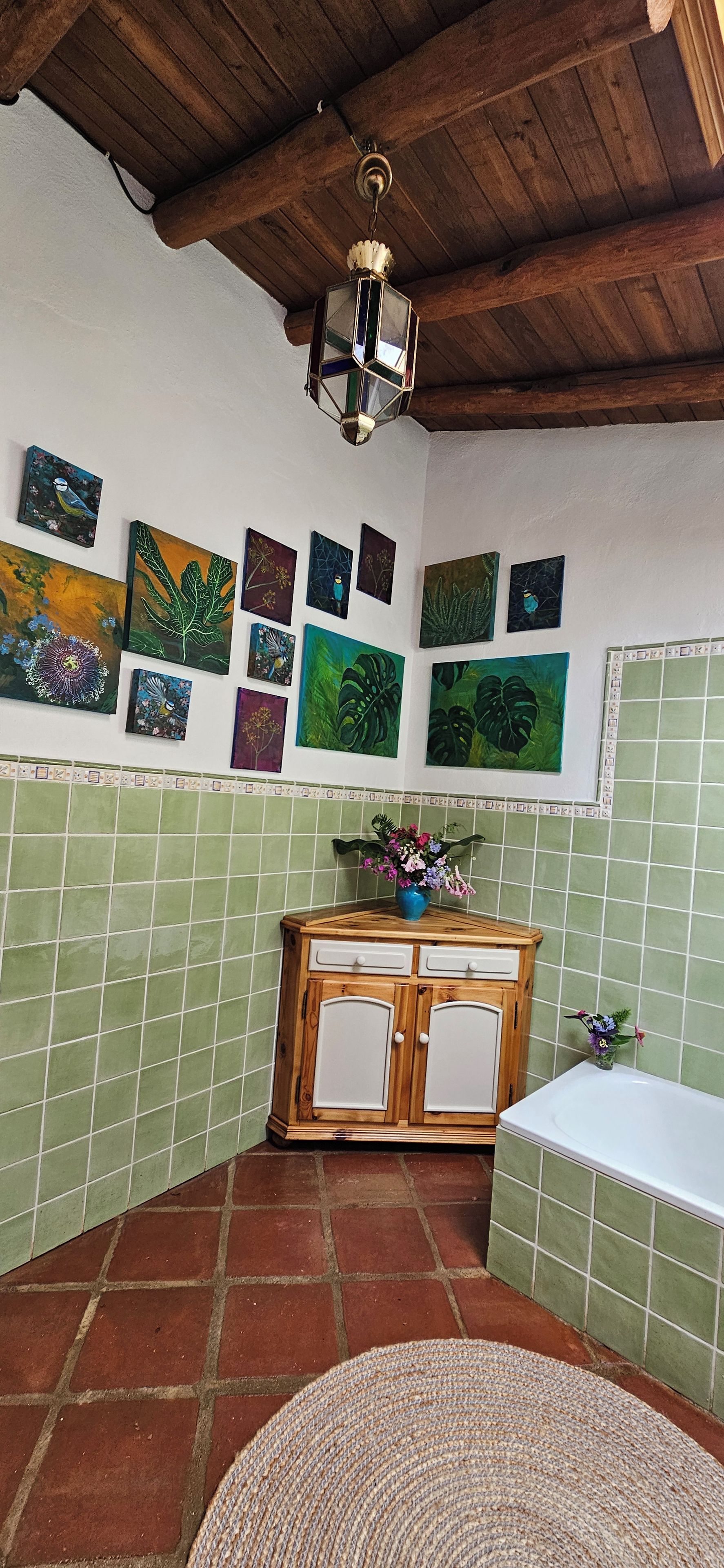 A bathroom with green tiles, a wooden cabinet, a white sink, and various wall art.