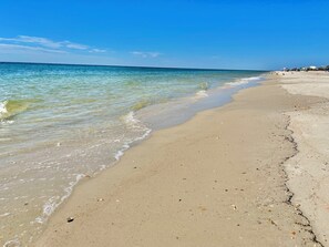 Una playa con agua cristalina, una orilla arenosa y algunos edificios a lo lejos.