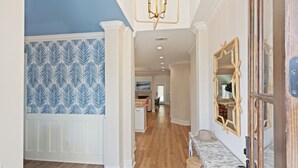 A hallway with patterned wallpaper, a wooden floor, and a mirror on the wall. - Executive  style home with 4 bedrooms and 3.5 baths. (Saint Simons Island)