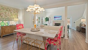 A dining area with a white table, clear chairs, and a chandelier. There is a wooden cabinet with green vases and a patterned wall behind the table. - Executive  style home with 4 bedrooms and 3.5 baths. (Saint Simons Island)