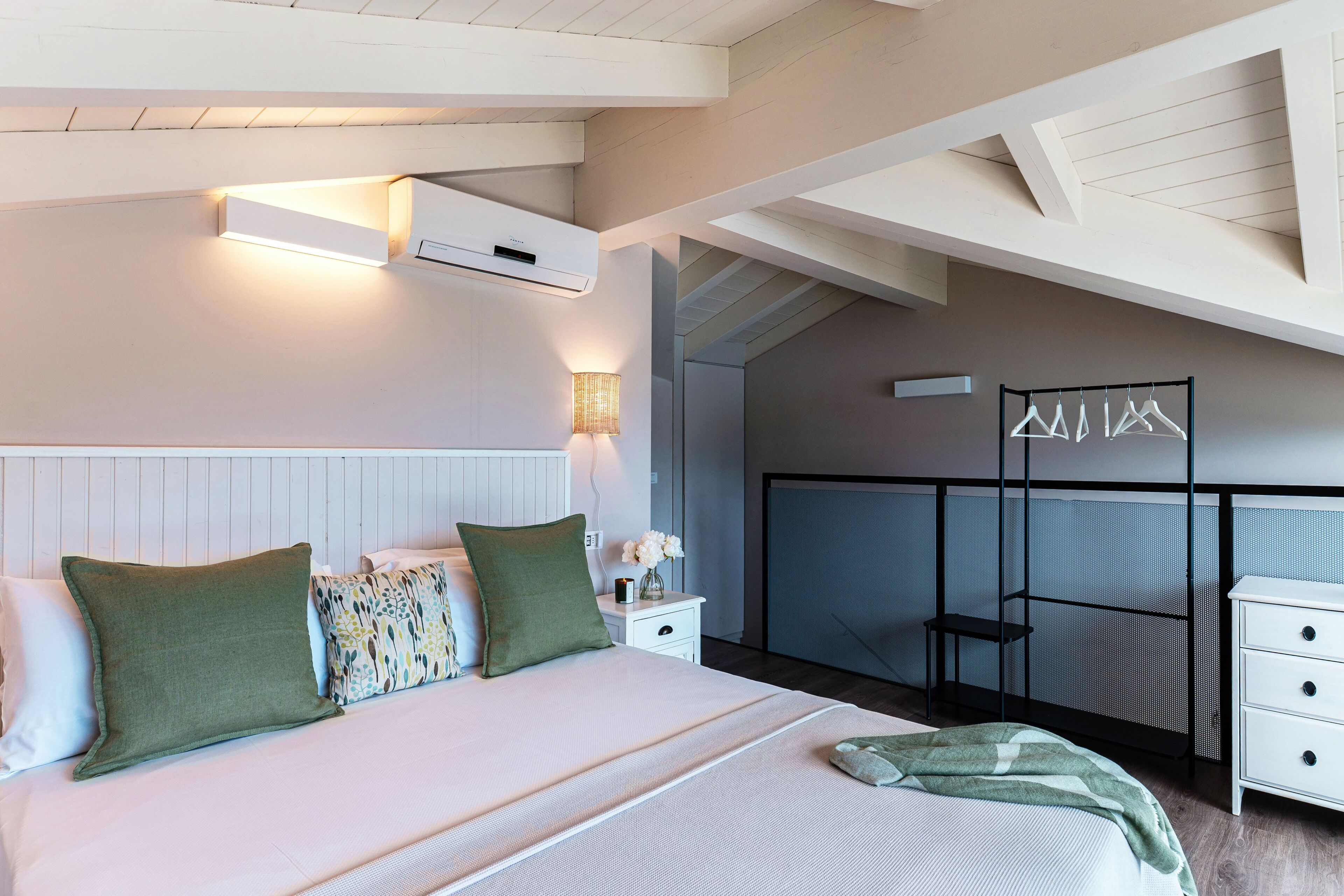 Ein Schlafzimmer mit einem Bett, Nachttischen, einer Lampe, einer Wand-Klimaanlage und einem Kleiderständer.