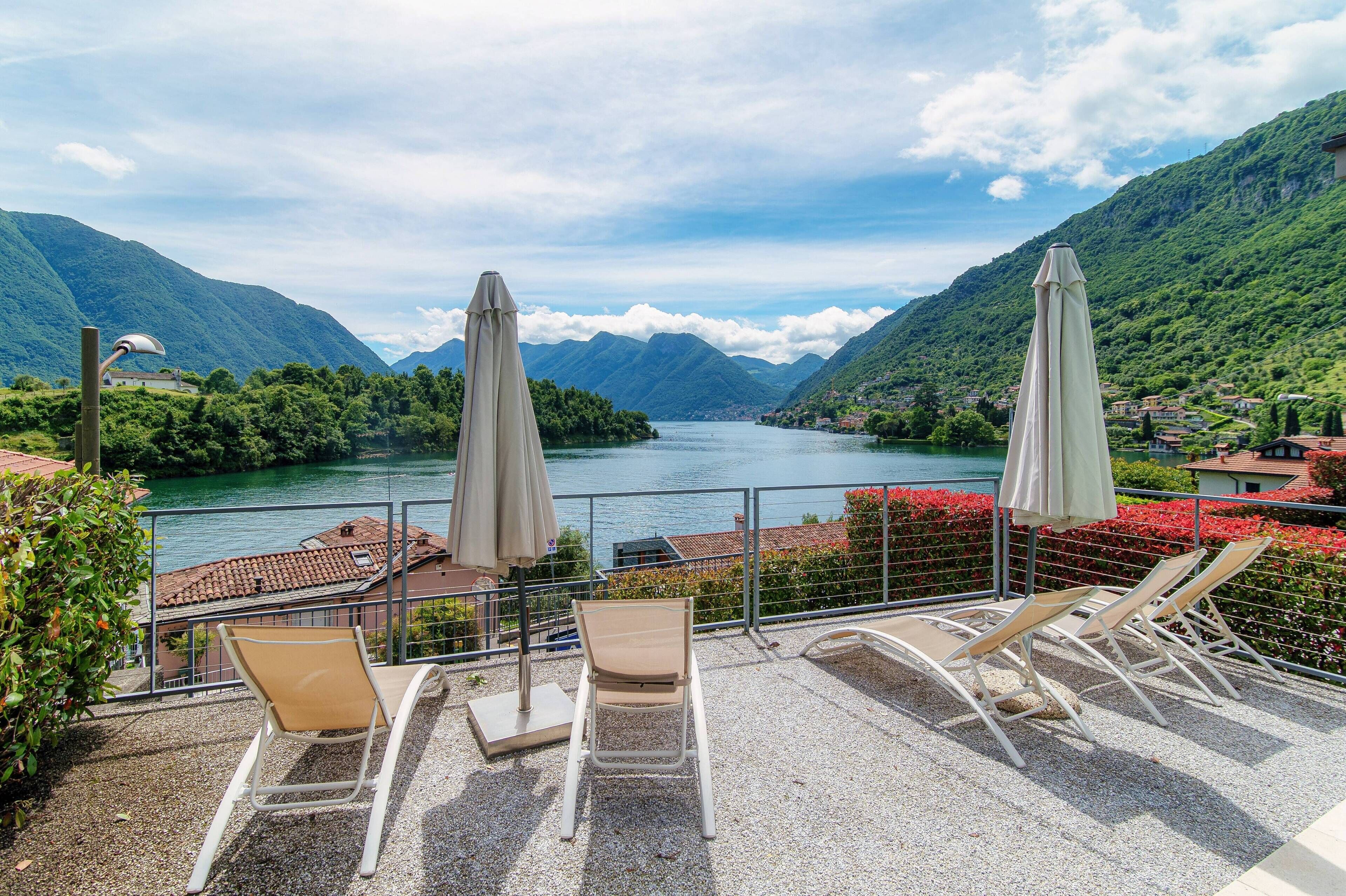Una terraza con mobiliario exterior y vistas a un lago rodeado de montañas.