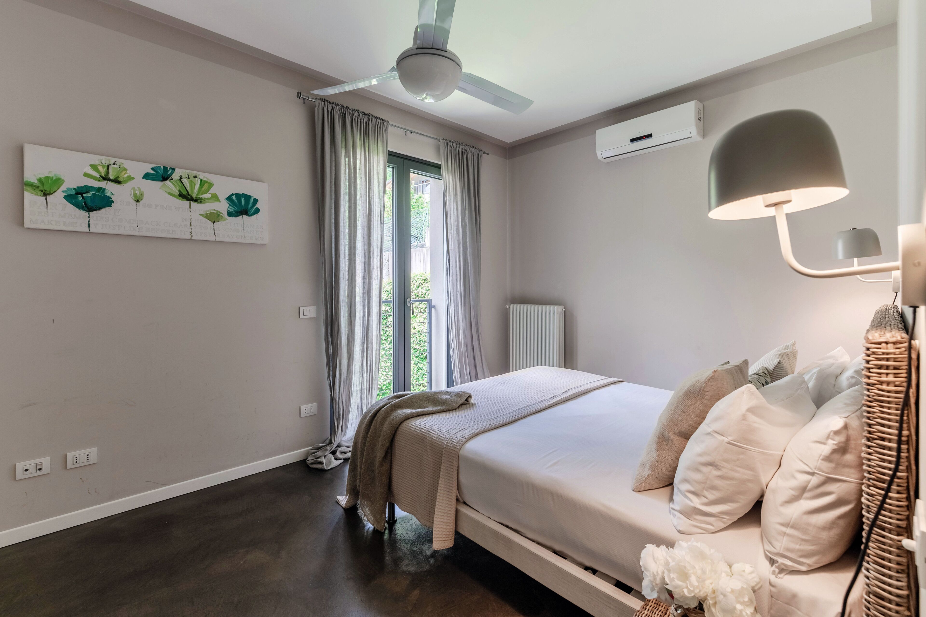 Une chambre à coucher comprenant un lit, un ventilateur de plafond, une fenêtre avec des rideaux, un radiateur et un climatiseur fixé au mur.