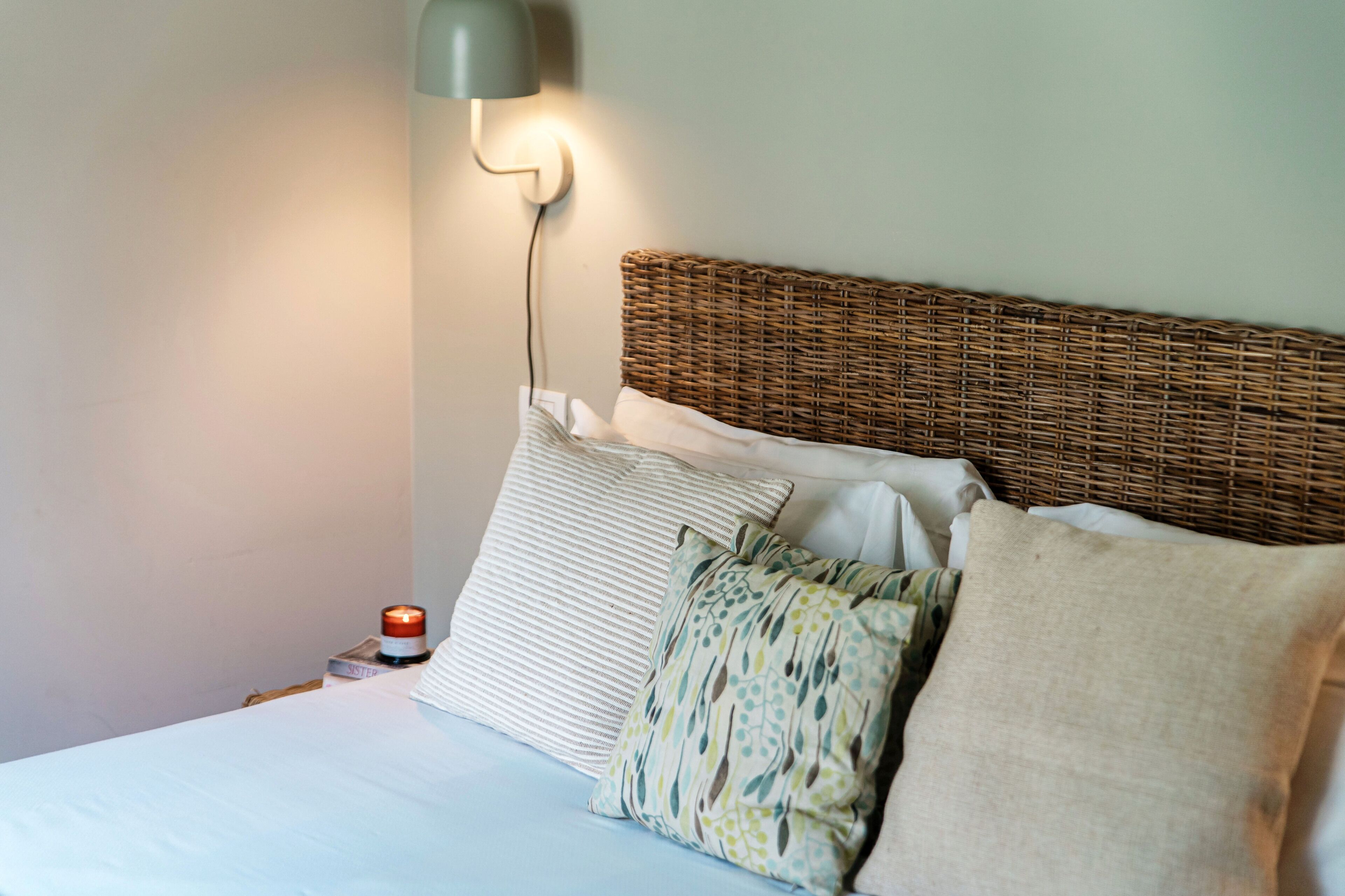 A bed with a wicker headboard, white bedding, and multiple pillows.
