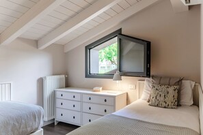 Un dormitorio con cama, mesita de noche, cómoda, ventana y techo con vigas de madera.