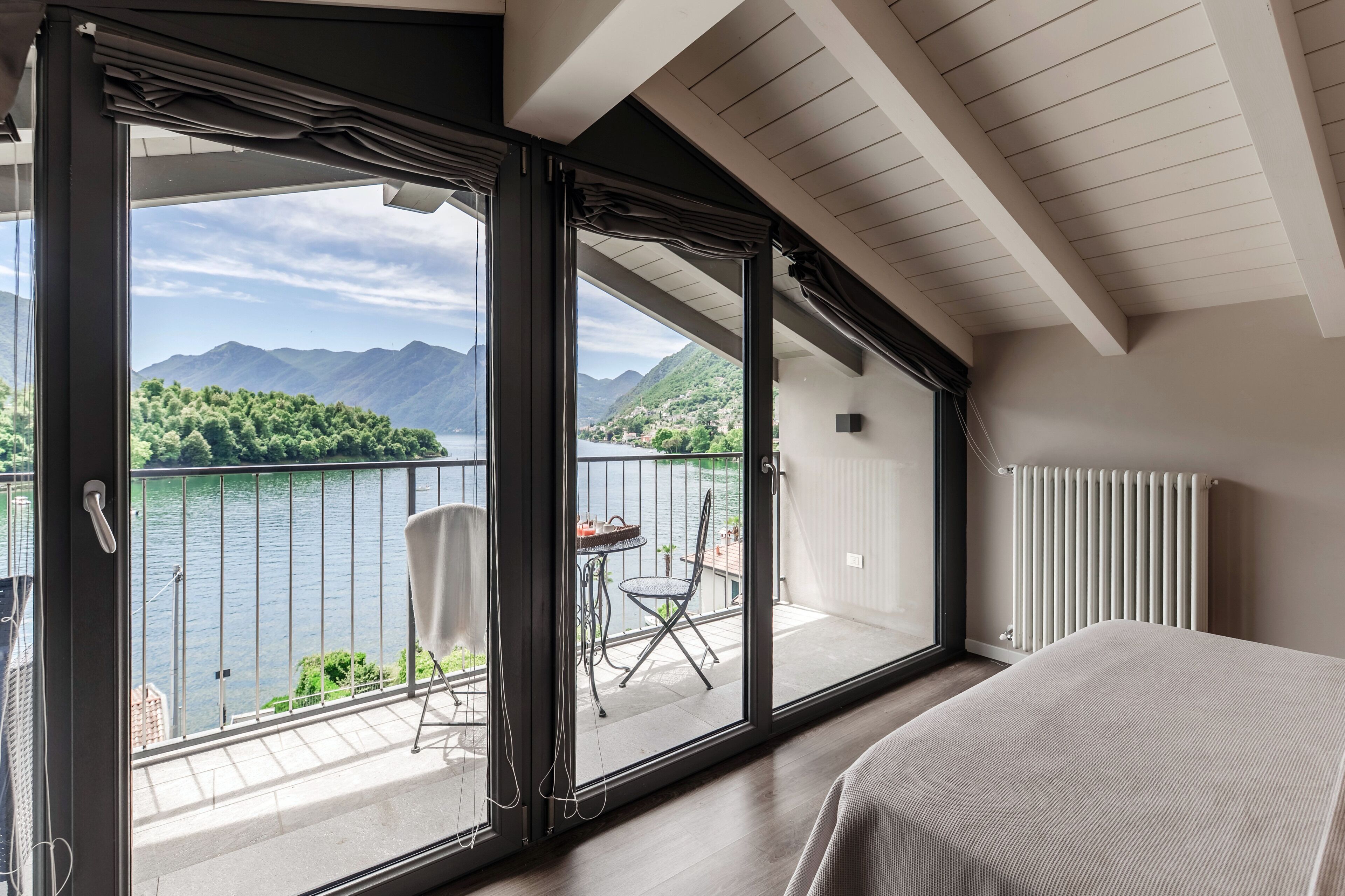 A bedroom with a large sliding glass door leading to a balcony with a view of a lake and mountains.