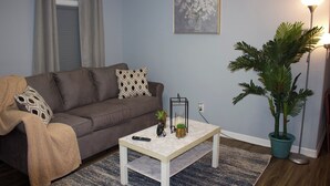 A living room with a grey sofa, a white coffee table, a potted plant, and a painting on the wall.