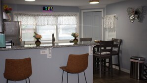 A kitchen with a built-in island, two bar stools, a refrigerator, and a clock on the wall.