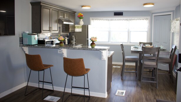 A modern kitchen with a bar area, two bar stools, and a dining table with chairs.
