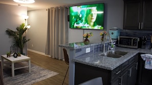 A modern kitchen with granite countertops, a built-in microwave, and a large flat-screen TV mounted above the island.