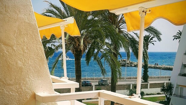 A balcony with yellow umbrellas, palm trees, and a view of the sea.