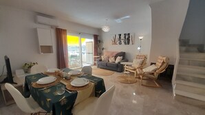 A dining area with a table set for four, a sofa, and a chair with a sun lounger.