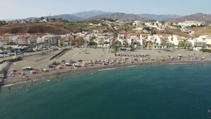 A coastal town with a beach, buildings, and mountains in the background.
