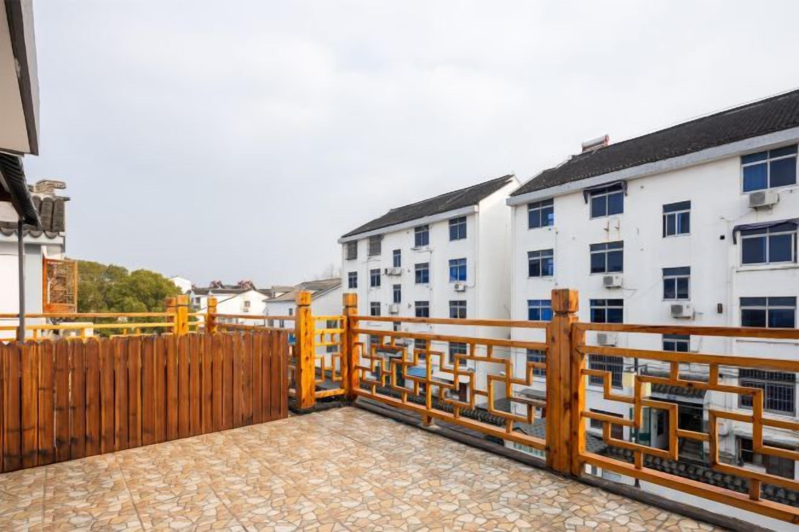 A rooftop terrace with a wooden fence, a tiled floor, and a view of a white building with multiple windows.