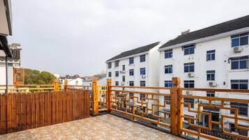 A rooftop terrace with a wooden fence, a tiled floor, and a view of a white building with multiple windows.