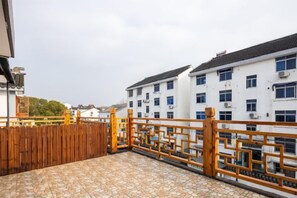 Terraza en la azotea con valla de madera, suelo de baldosas y vista a un edificio blanco con múltiples ventanas.