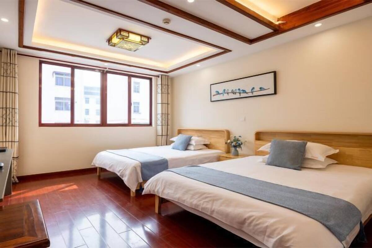 A hotel room with two beds, wooden flooring, a large window, and a ceiling light fixture.