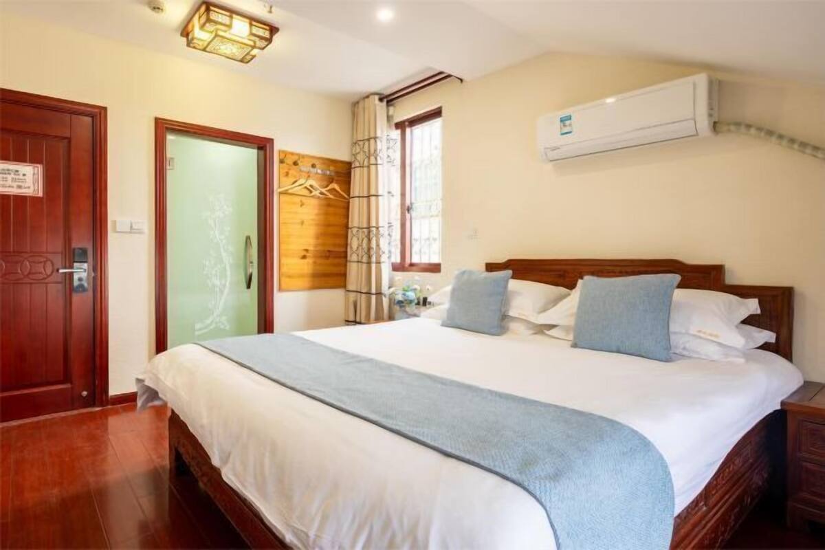 A hotel room with a wooden bed, a white wall, a window, and an air conditioning unit.
