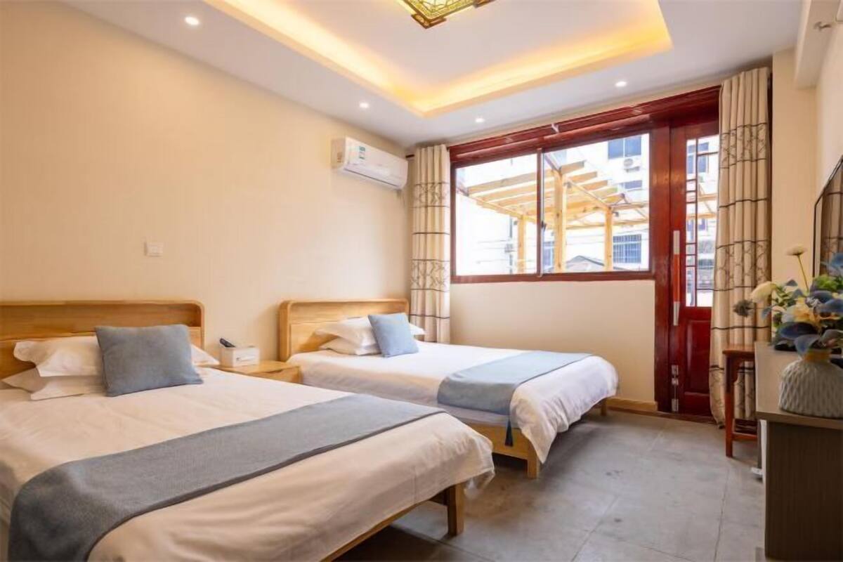 A hotel room with two beds, a window with curtains, an air conditioning unit, and a wooden headboard.